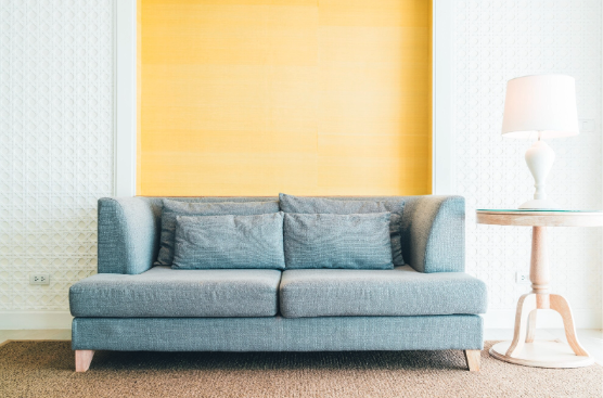 A gray couch in front of a yellow wall.